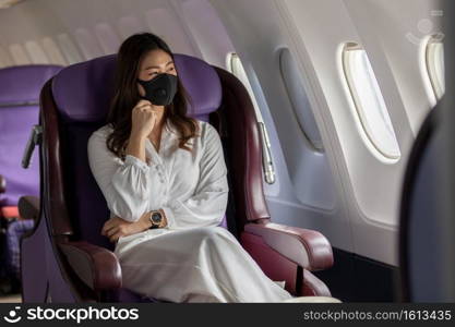 Asian young woman wearing protective mask sitting near windows at first class on airplane during flight,Traveling and Business during COVID-19 virus pandemic concept