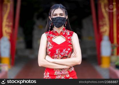 Asian young woman wearing red cheongsam dress traditional decoration and wear protective mask germs for Chinese New Year Festival at shrine,Prevention of the spread of COVID-19 virus