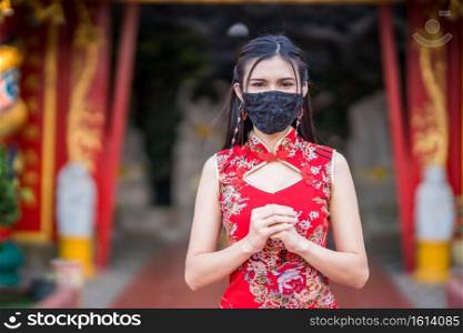 Asian young woman wearing red traditional Chinese cheongsam decoration and wear protective mask germs for Chinese New Year Festival at shrine,Prevention of the spread of COVID-19 virus
