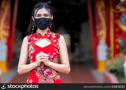 Asian young woman woman wearing red cheongsam dress traditional decoration and wear protective mask germs for Chinese New Year Festival at shrine,Prevention of the spread of COVID-19 virus