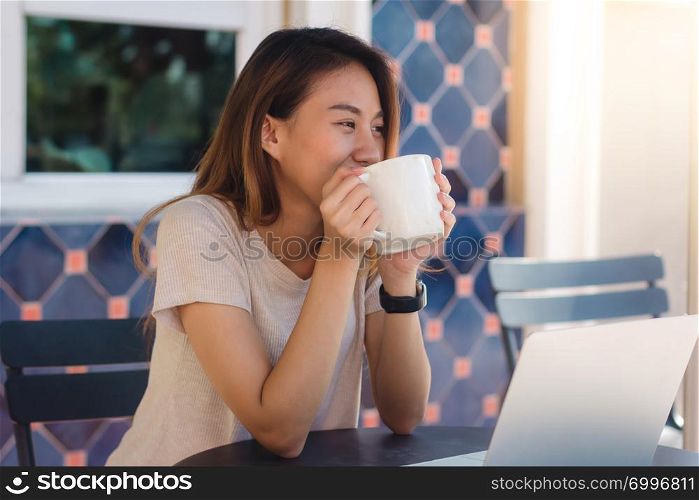 Asian young women in smart casual clothes working sending email on laptop and drinking coffee while sitting in cafe. Lifestyle women communication and working in coffee shop concept.