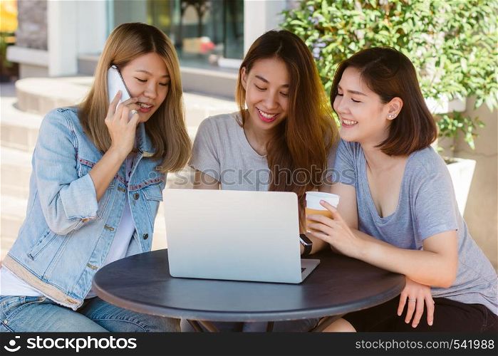 Asian young women working on laptop using and looking smartphone and drinking coffee while sitting in cafe. Lifestyle women communication and working in coffee shop concept.