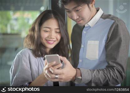 asian younger man and woman looking to smart phone screen toothy smiling face happiness emotion