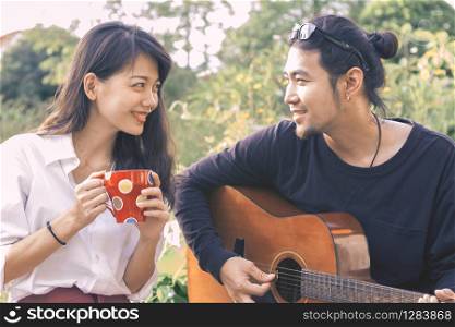asian younger man and woman playing guitar singing song in park