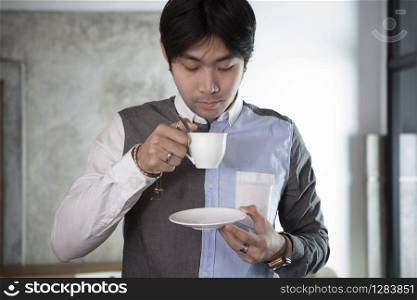 asian younger man drinking hot beverage in white cup