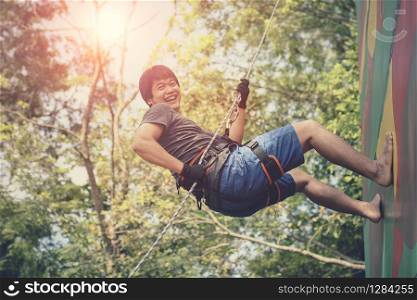 asian younger man hanging on clip hiking safety rope and laughing with happiness emotion