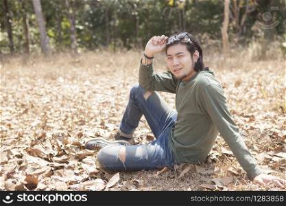 asian younger man sitting on dry leaves field with smiling face