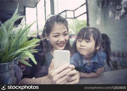 asian younger woman and children looking to smart phone screen at home living room