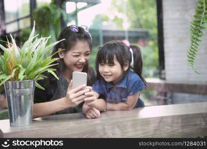 asian younger woman and children looking to smart phone screen at home living room