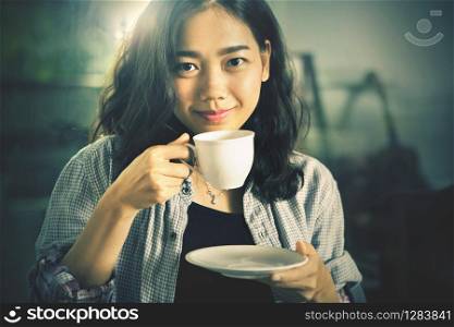 asian younger woman drinking hot coffee in white cup