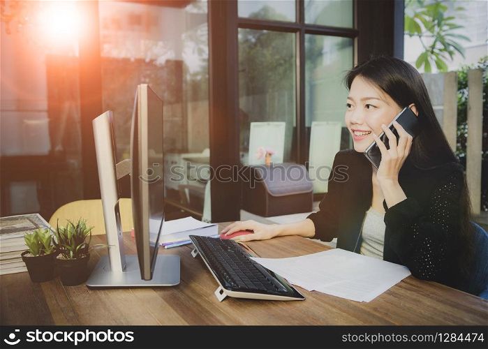 asian younger woman taking on mobilephone and computing in working office