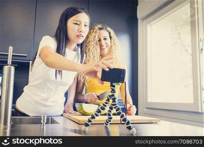 asiatic girl and caucasian girl making a video for a blog with fruit in the kitchen