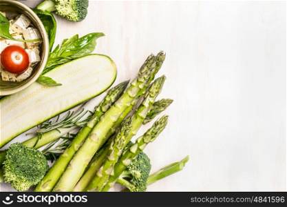 Asparagus and green vegetables on white wooden background, top view, border