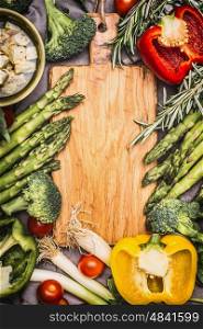 Asparagus and vegetables ingredients around blank wooden cutting board, top view, frame