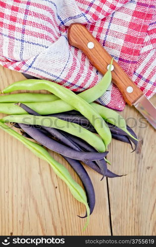 Asparagus beans green and purple, napkin, knife on background wooden plank