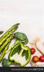 Asparagus, green paprika,broccoli and tomatoes on white wooden background, top view, border, vertical. Healthy or diet food and cooking concept