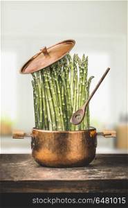 Asparagus in cooking pot with wooden spoon on rustic kitchen table , front view. Healthy vegetarian food and eating concept