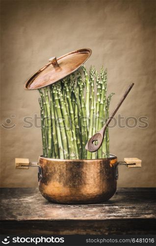 Asparagus in cooking pot with wooden spoon on rustic table , front view. Healthy vegetarian food and eating concept