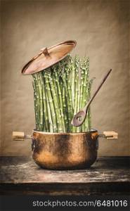 Asparagus in cooking pot with wooden spoon on rustic table , front view. Healthy vegetarian food and eating concept