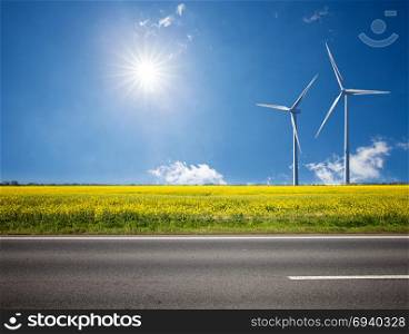 Asphalt road among the summer sunny field with wind power electricity turbines. Alternative electricity power station