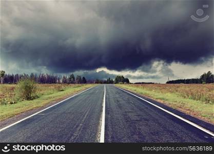 asphalt road and dark thunder clouds over it .