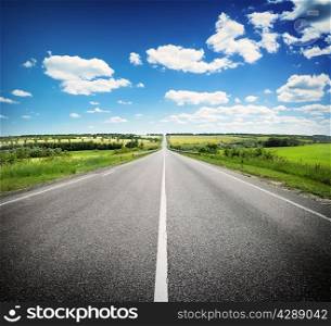 Asphalt road in field under blue cloudy sky