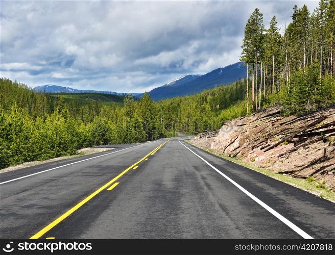 Asphalt road in mountains with forest and cloudy sky