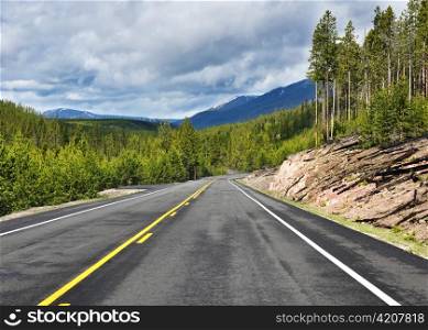 Asphalt road in mountains with forest and cloudy sky