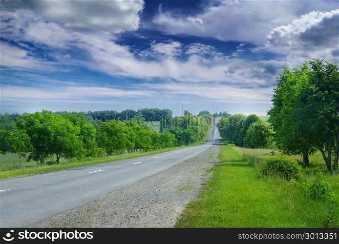Asphalt road in the countryside through green summer fields and a bright blue sky with white clouds.