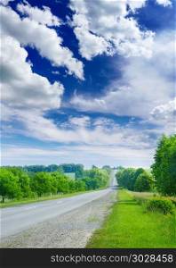 Asphalt road in the countryside through green summer fields and a bright blue sky with white clouds.. Asphalt road in the countryside through green summer fields