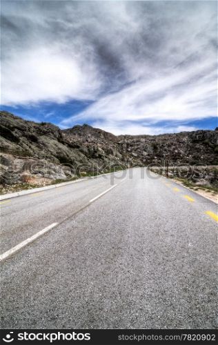 Asphalt road in the mountains and blue sky with clouds.