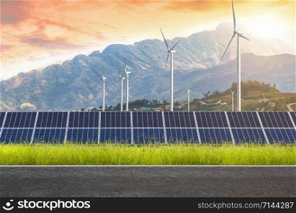 Asphalt road with solar panels with wind turbines against mountanis landscape against sunset sky,Alternative energy concept