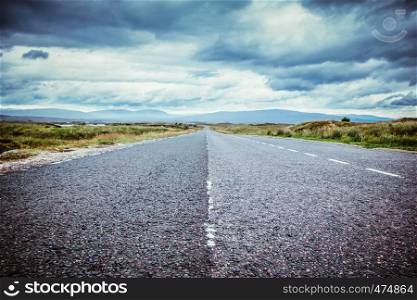 Asphalted, dramatic road in Scotland. Nobody and cloudy sky.