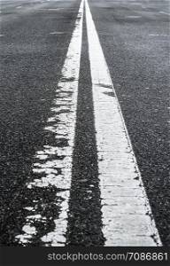 Asphalted road with two continuous faded white strips. White road divider lines of a highway. Long banner format. Two-way asphalt road, close up of the dividing road strip.. White road divider lines of a highway. Long poster format.