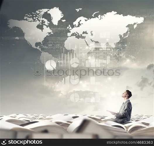 Aspiration for knowledge. Young businessman sitting in pile of books with one in hand and looking at graphs above