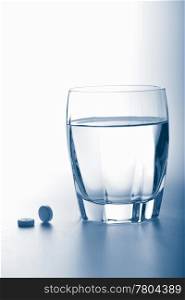 aspirin pills and glass of water toned blue