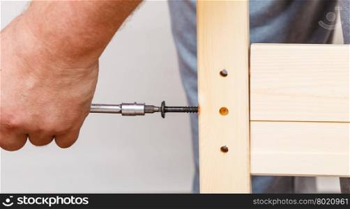 Assembling wood furniture using scredriver. DIY.. Human hand assembling wood furniture using screwdriver. DIY enthusiast. Home improvement.