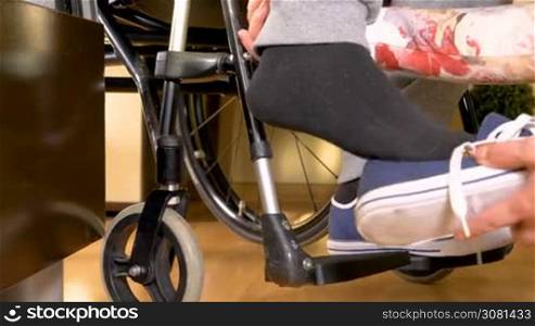 Assistance for a disabled man in wheelchair, tying shoes. Closeup