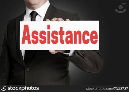 Assistance placard is held by businessman.. Assistance placard is held by businessman