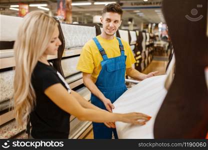 Assistant and female customer choosing wallpapers in hardware store. Seller in uniform and woman in diy shop, shopping in building supermarket