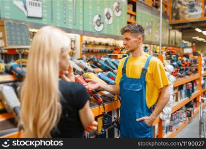 Assistant and female purchaser in hardware store. Seller in uniform and woman in diy shop, shopping in building market. Assistant and female purchaser in hardware store