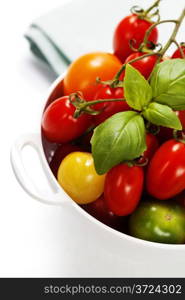 Assorted colorful tomatoes and vegetables in colander on white background - healthy eating concept