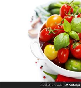 Assorted colorful tomatoes and vegetables in colander on white background - healthy eating concept