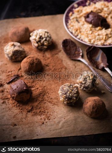 Assorted dark chocolate truffles with cocoa powder, biscuit and chopped hazelnuts over baking paper, selective focus