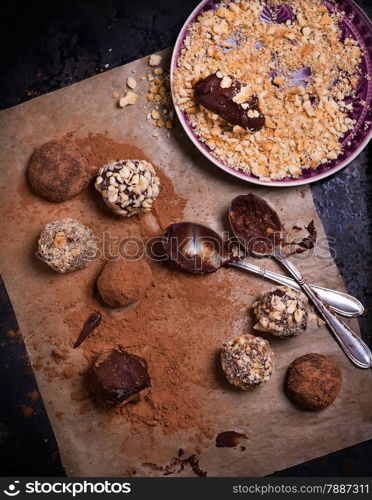Assorted dark chocolate truffles with cocoa powder, biscuit and chopped hazelnuts over baking paper, selective focus, top view