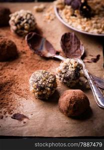 Assorted dark chocolate truffles with cocoa powder, biscuit and chopped hazelnuts over baking paper, selective focus
