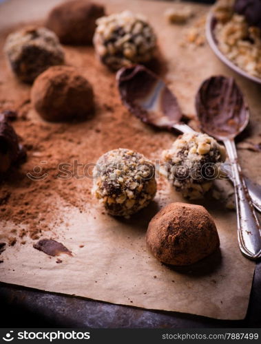 Assorted dark chocolate truffles with cocoa powder, biscuit and chopped hazelnuts over baking paper, selective focus