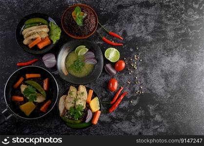 Assorted food and dishes of vegetables, meat and fish on a black stone background. Top view.