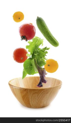 Assorted fresh vegetables falling into a wooden salad bowl isolated on white background
