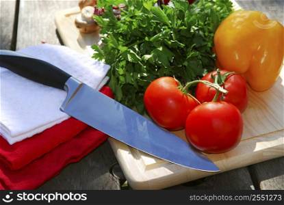 Assorted fresh vegetables on cutting board on rustic table with a chef knife